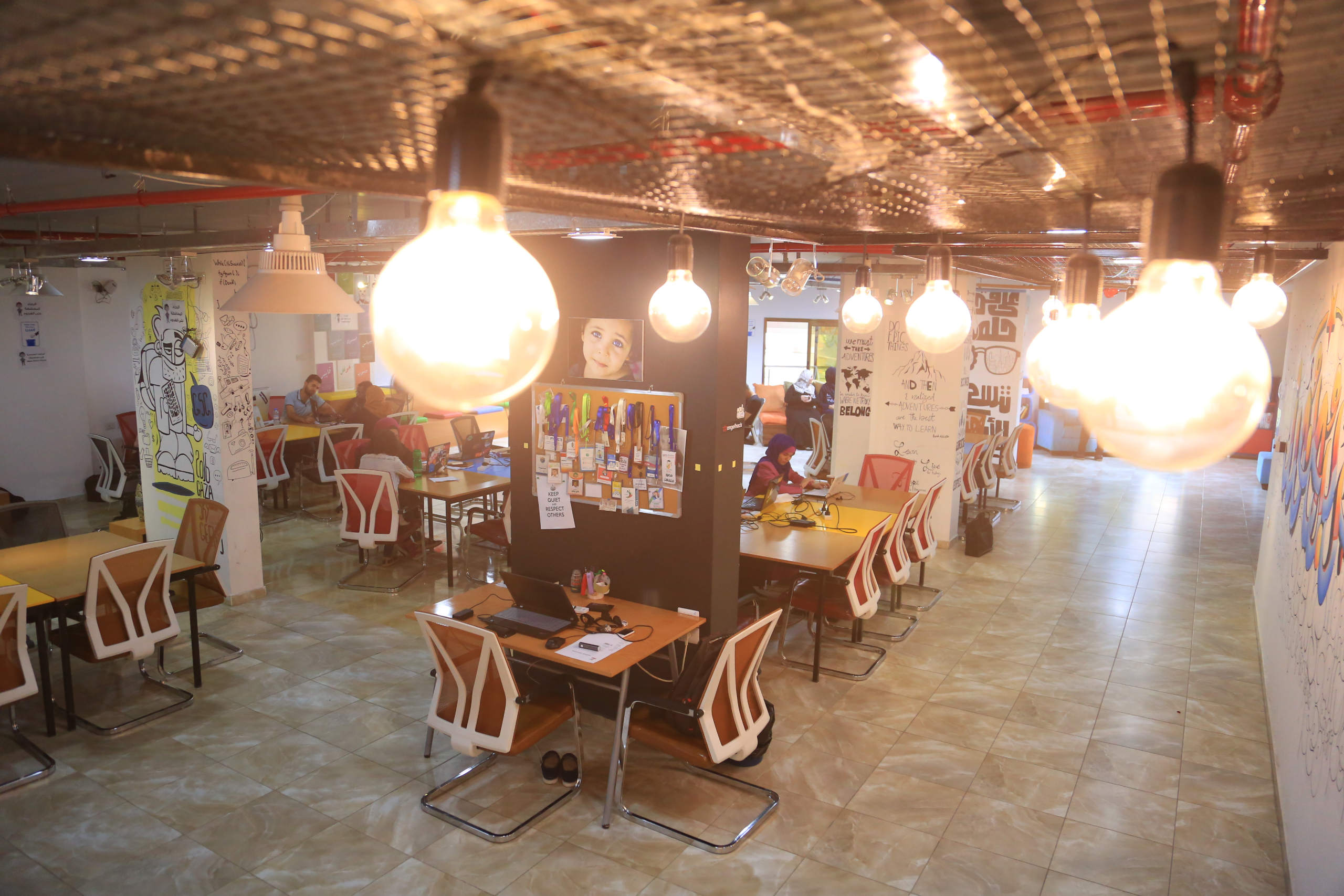 Ambiente interno de coworking com mesas, computadores e pessoas trabalhando