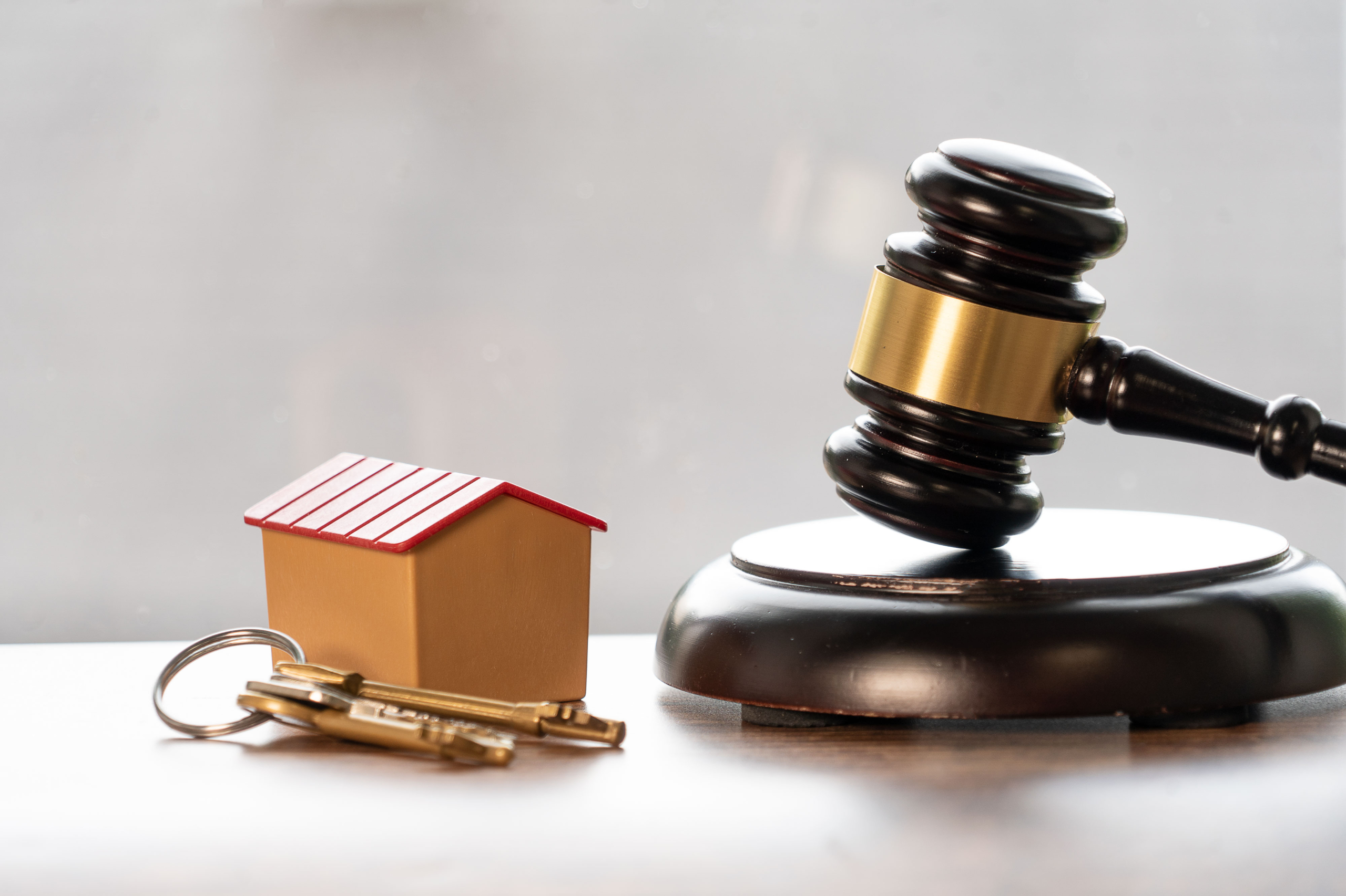 Martelo de juiz, miniatura de casa e chaves representando a segurança jurídica da compra imobiliária